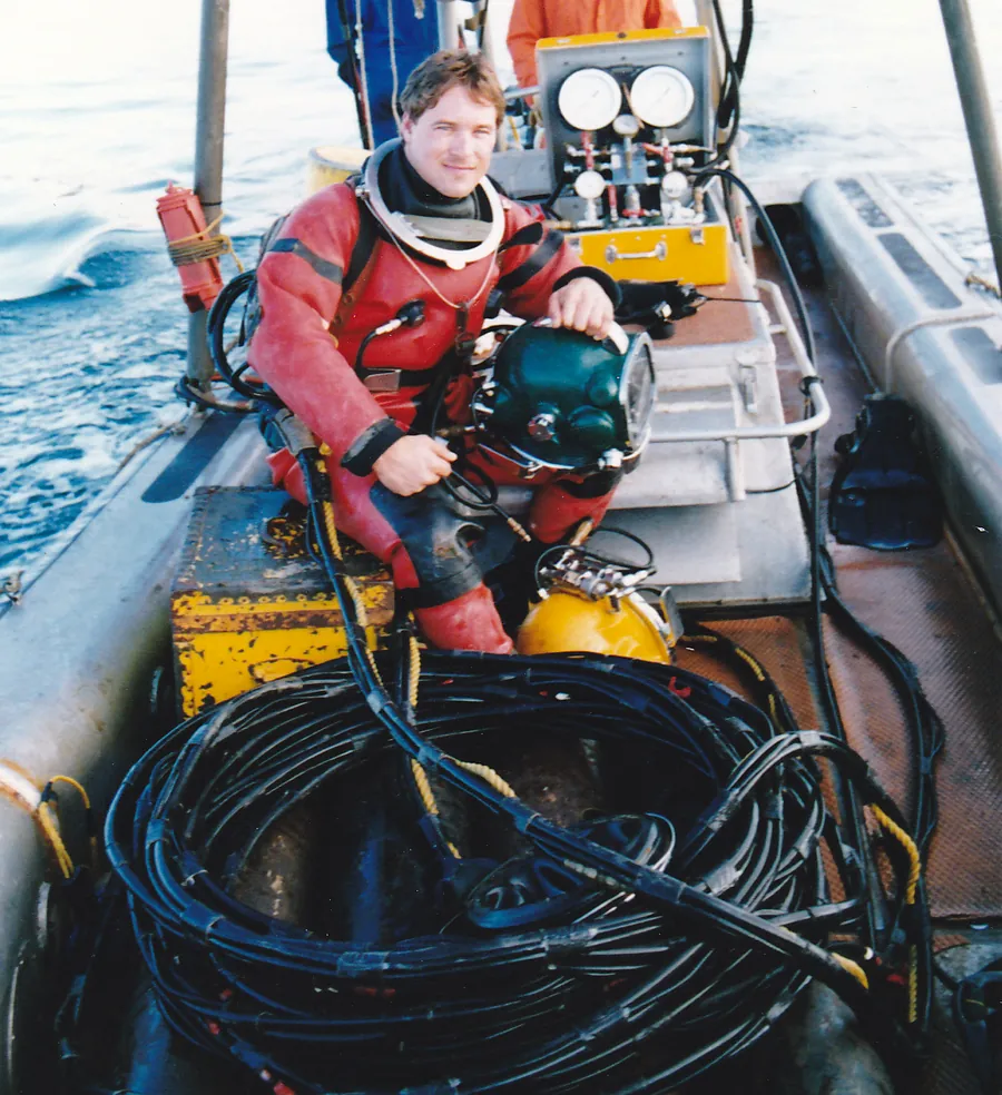 A young Ted in a dive boat with his helmet and umbilical hoses