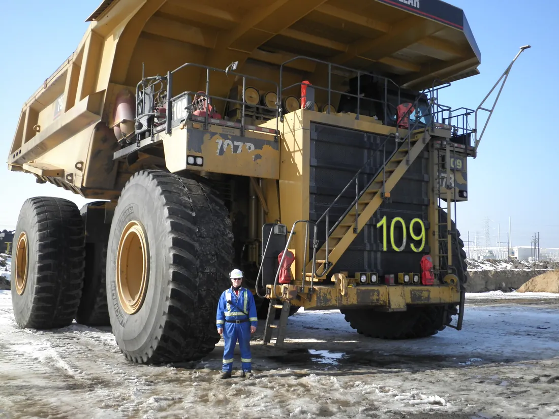 Ted in coveralls beside a giant oil sands haul truck