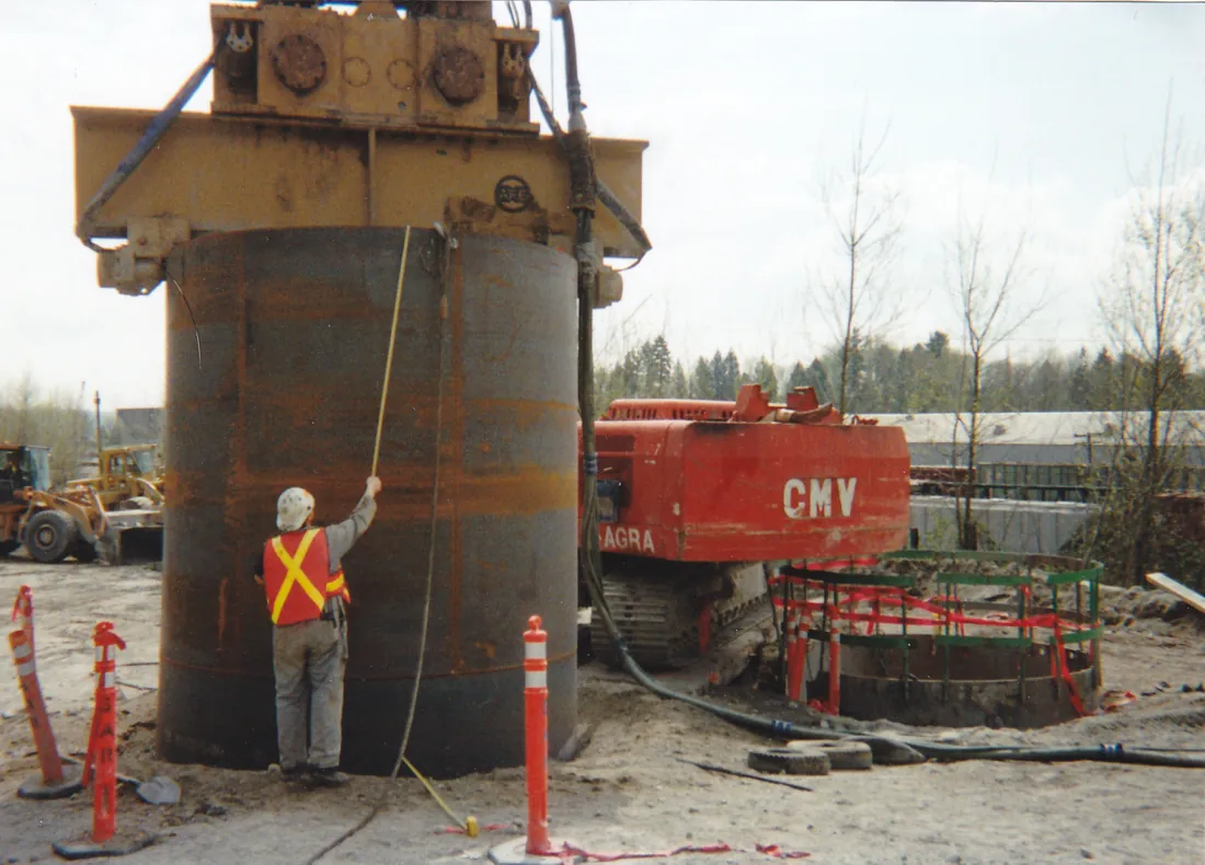 A worker measuring a steel pile under a pile-driving hammer